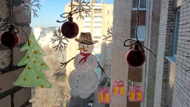 Painting snowman, christmas tree and snowflakes on the window glass. Winter picture on the window with christmas balls.
