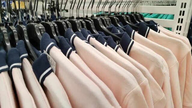 Polo shirts on a hanger in a clothing store or shopping mall. A peach or beige polo with a blue collar in a sports store. Lots of light T-shirts. Close-up.