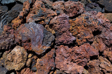 View of volcanic rocks from past volcano eruption on Lanzarote island. Beautiful red brownish and black rough texture stones made by lava. Close up view of basaltic lava rocks. Canary Islands, Spain.