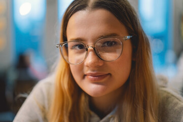 Portrait of a teenage girl wearing glasses and looking at the camera. Close up face of happy girl in glasses smiling at school. Confident and satisfied student in glasses in the office.