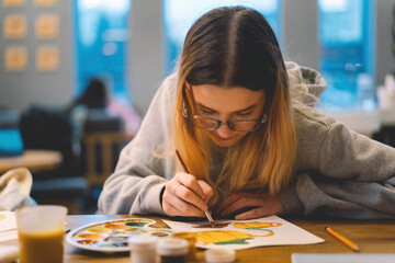 Pretty teenage girl draws a picture with poster paint. Front view of a drawing of a girl with a palette in her hand. A smiling young teenage girl draws a picture