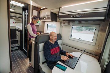 Happy woman cooking food while man using laptop in camper van