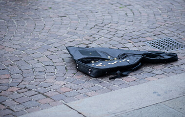 A street artist's guitar case with coins on a city street in Italy