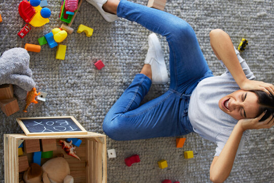 Tired, Stress And Frustrated Mom With Fatigue And Headache Cleaning Children Toys. Above View Of Mama And Woman Scream From Kids Mess In A Home Living Room Feeling Overwhelmed Burnout From Motherhood