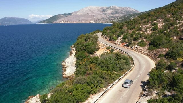 Drone following the car moving by the sea curved road near a tranquille waves on the Greek coast on Cephalonia island. Transportation, nature 4K aerial video concept.