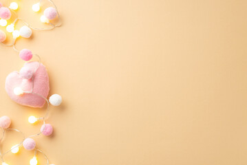 Saint Valentine's Day concept. Top view photo of soft heart shaped toy light bulb garland and fluffy pompons on isolated pastel beige background with copyspace