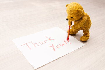 紙にクレヨンでthank you!!と書くテディーベアー
