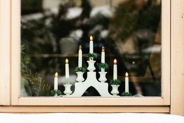 Traditional Swedish Christmas white candlestick bridge with lights by a wooden window with snow on the windowsill