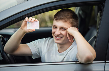 Contented and joyous student driver shows his license out of the car window