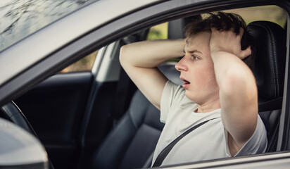 Shocked and scared student driver keeps messing hair with hands while stands at the steering wheel....