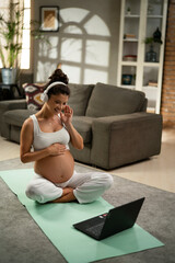 Beautiful pregnant woman practising yoga at home. Young woman listening music while exercise at home.