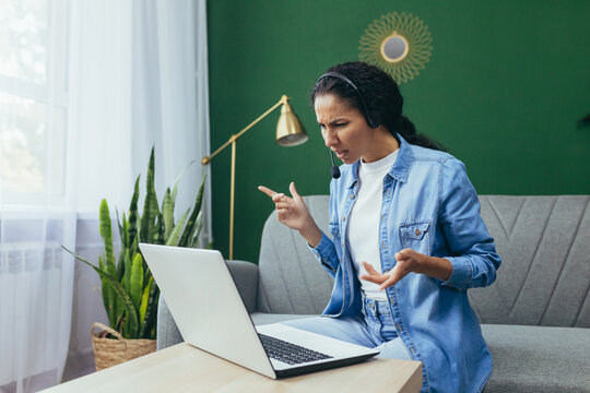 Portrait of frustrated and upset woman at home, Hispanic woman working remotely looking at laptop at work and video call headset sitting on sofa in living room.