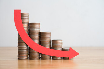 Stack of coins bar chart and red curve graph trending downwards with white wall background on wooden table copy space. Economy recession crisis, inflation, stagflation, business and financial loss.