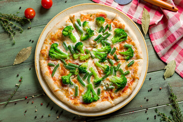 Pizza with vegetables, cheese and broccoli on green wooden table top view