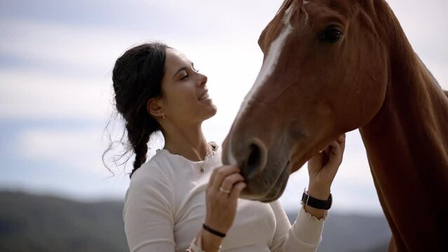 Authentic close up shot of a pretty young woman is caressing and kissing a brown horse laughing and smiling happily