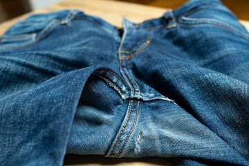Naklejka premium Hole in jeans. Worn, old denim trousers on a wooden table. 