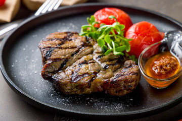 Fried pork loin with sauce and grilled tomatoes on black plate