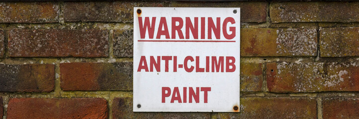 Warning sign on brick wall for Anti-Climb paint in panorama format