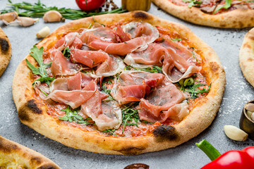 Pizza with Parma ham and arugula on wooden board on grey table