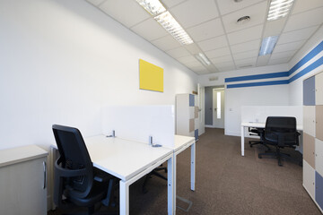 Several empty corporate work desks with divider screens and filing cabinets