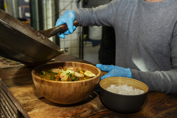 An Asian chef preparing a bowl of ramen with prawns, pumpkin noodles and a small bowl of white rice