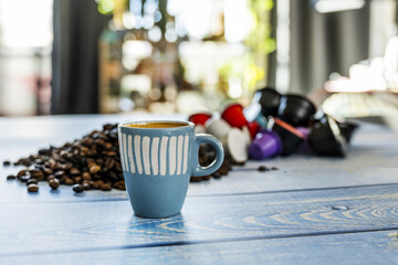 Coffee still life with a blue porcelain cup with assorted capsules and blurred coffee beans on a blue wooden plank table