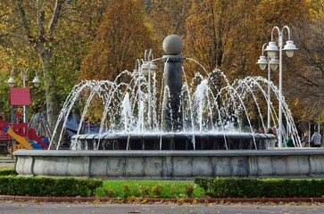 fuente con agua y detras parque infantil y arboles con hojas en Bilbao