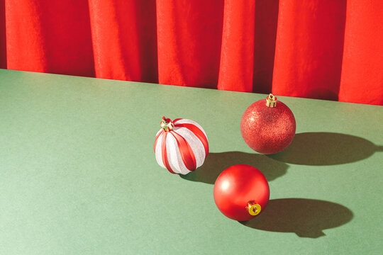 Vintage retro scene with red Christmas baubles on deep green table and red plush curtain. Creative xmas composition with copy spece.