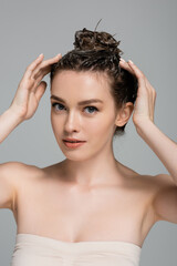 young woman with foam on head washing hair and looking at camera isolated on grey