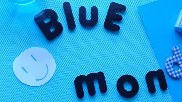 4k v&iacute;deo. Slow motion Letras de Blue Monday en fondo azul con una cara sonriente animada y material de papeler&iacute;a azul. Lunes azul alegre vista cenital