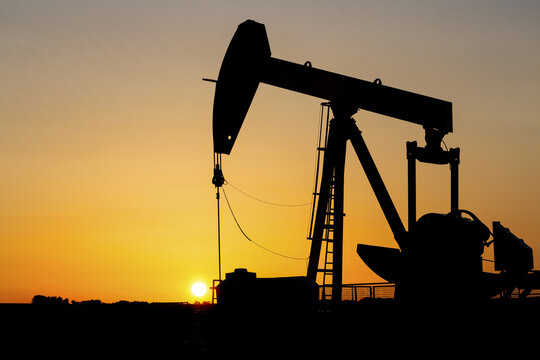 Silhouette of a pumpjack at sunrise with a glowing warm sky, West of Airdrie; Alberta, Canada