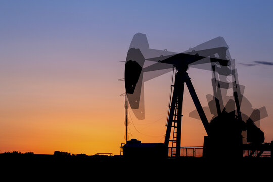 Multi exposure of a pumpjack silhouetted at sunrise with a glowing warm sky, West of Airdrie; Alberta, Canada