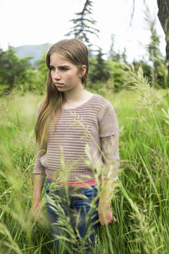 A preteen girl stands in tall grass in a field; Salmon Arm, British Columbia, Canada