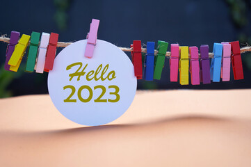Hello 2023. New Year 2023 concept with golden text on white circle paper and colorful wooden clips...