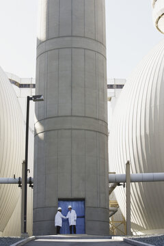 Two scientists shaking hands in front of a digester tank