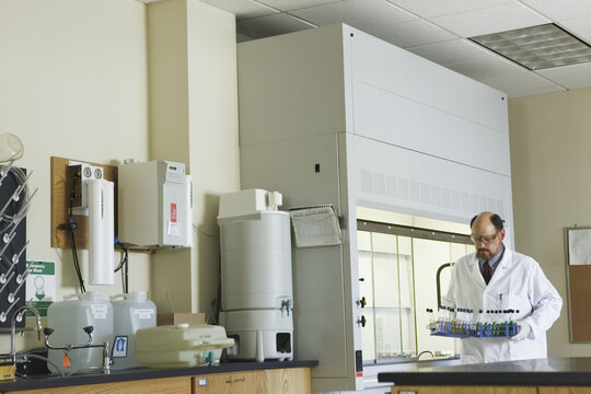 Scientist carrying racks of test tubes from fume hood
