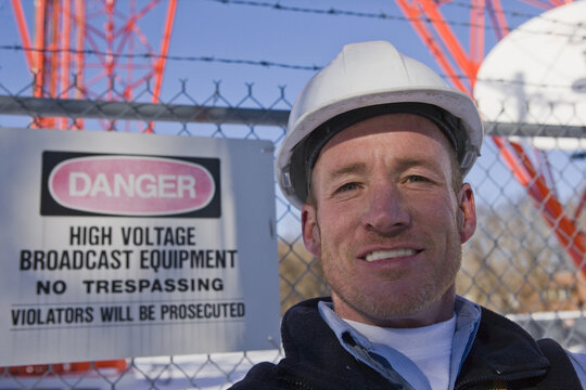 Cable lineman with a warning sign in front of a microwave tower