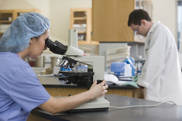 Female lab technician analyzing a sample through a microscope