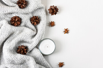 Winter cozy composition of knitted sweaters, candles, pine cones, stars of star anise.