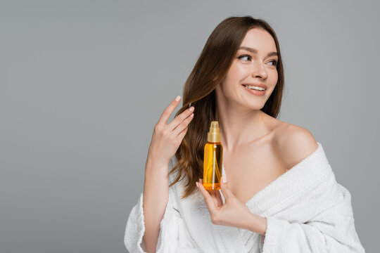 Cheerful Young Woman Holding Bottle With Hair Oil Isolated On Grey