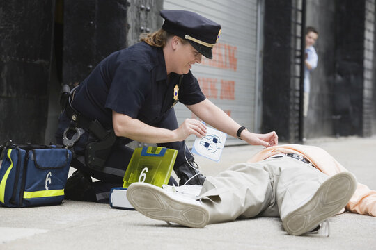 Woman police officer administering defibrillator to a senior man