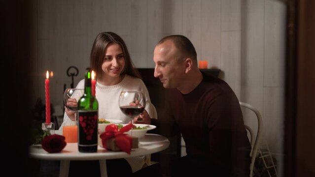 Affectionate couple enjoying date at home, celebrating Valentine's Day together, lovers having romantic dinner, eating and smiling to each other