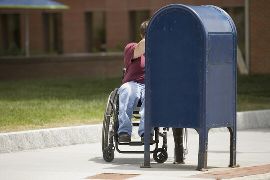 Woman sitting in a wheelchair and putting mail into a mailbox