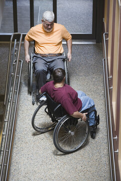 High angle view of a mature man with Muscular Dystrophy and a young woman sitting on wheelchairs in a library