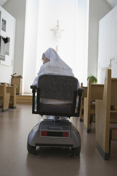 Rear view of a nun sitting in a motorized wheelchair in a church