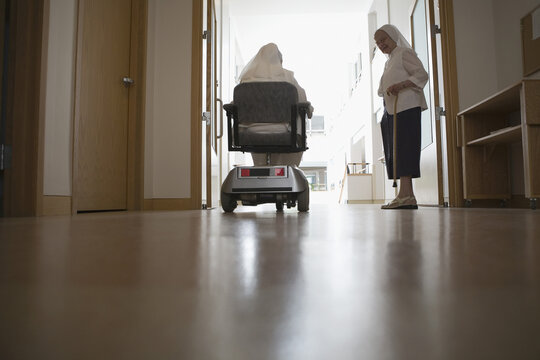 Rear view of a nun sitting in a motorized wheelchair with another nun standing beside her in a church