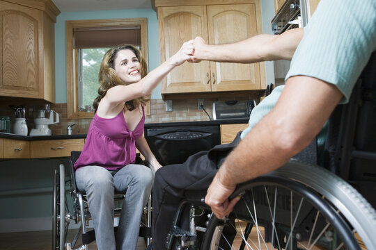 Mid adult woman sitting in a wheelchair and holding the hand of a man