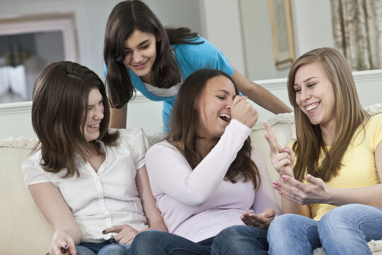 Four teenage girls sitting on a couch at home playing the rock, paper, scissors game