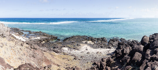 Large panorama d'un lagon turquoise et émeraude avec vagues déferlant sur la barrière de corail