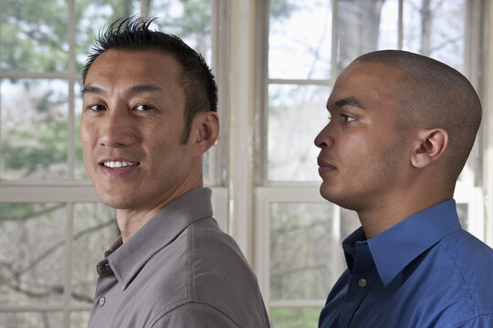 Portrait Of The Side View Of Two Young Businessmen Standing Facing Left, One Looking At The Camera